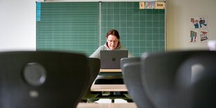 Eine Frau sitzt an einem Laptop in einem leeren Klassenraum,