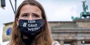 Luisa Neubauer trägt eine Maske mit der Aufschrift "Kein Grad weiter" und blickt ernst nach oben