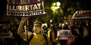 Menschen mit Mundschutz protestieren in der Nacht mit Plakaten.