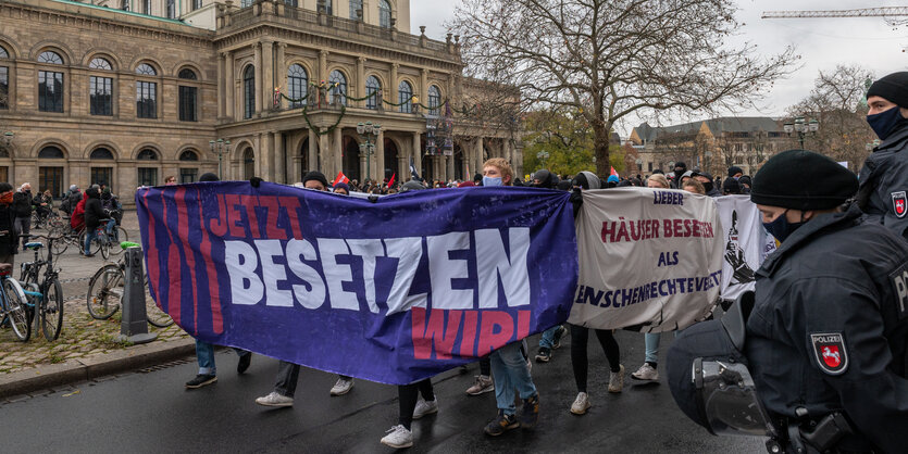 Menschen mit einem Transparent laufen an einem historischen Gebäude vorebei, rechts Polizisten