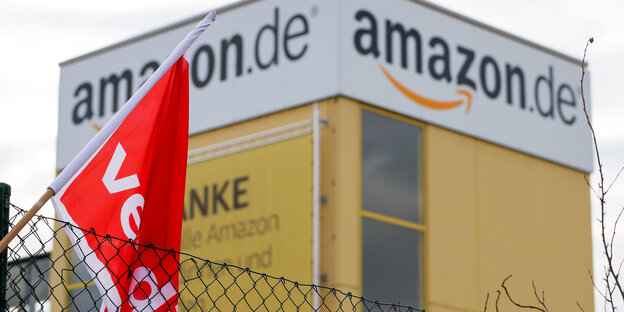 Eine Verdi-Fahne hängt während eines Streiks am Zaun des Amazon-Versandzentrums Leipzig