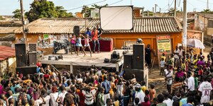 Kuduro-Outdoor-Party in Angola - Kinder tanzen hinter ihnen ein Mann mit Mikrofon und DJs - vor der Bühne Konzertgäste