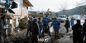 Beim Dreh der Serie "Die Fallers" stehen viele Menschen in ARD-Jacken draußen vor einem Holzhaus, während eine Kamera auf einem Gleis gefahren wird. Es liegt Schnee