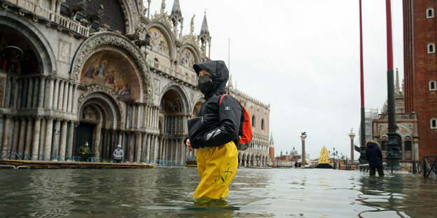 Eine Frau in wasserfester Kleidung watet durch's Wasser auf dem überfluteten Markusplatz in Venedig