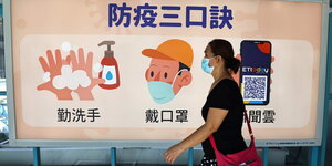 In Taipeh trägt eine Frau an einer U-Bahn-Station eine Gesichtsmaske - auf einer Tafel stehen Verhaltensregeln die vor dem Coronavirus schützen können