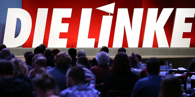 Delegierte der Linkspartei sitzen im Plenum vor dem Logo der Partei