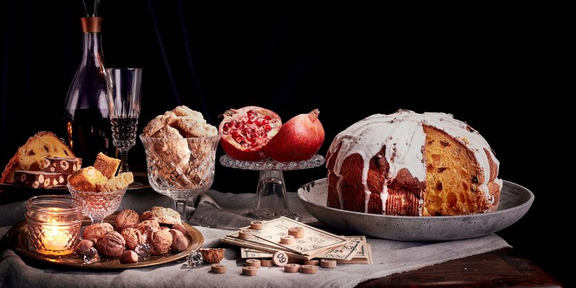 Ein wie gemalt aussehender Tisch, mit Weihnachtskuchen, Granatapfel, Nüssen und Karaffe