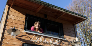 Eine Frau guckt aus dem Fenster ihres Holzhauses