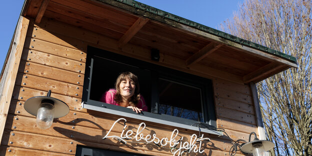 Eine Frau guckt aus dem Fenster ihres Holzhauses