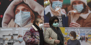 Zwei Frauen mit Mund-Nasenschutz gehen an Plakaten auf einer Straße in Madrid vorbei