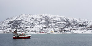 Ein Fischerboot kehrt von einer Reise in die Barentssee in den winzigen Hafen von Sommaroya in Nordnorwegen zurück