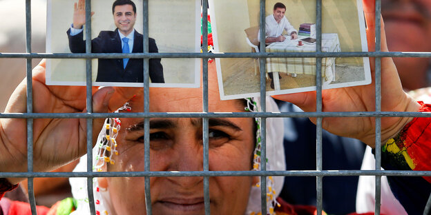 Eine Frau hält zwei Fotos von Selahattin Demirtas gegen ein Gitter.