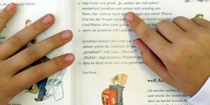 Buchstabe für Buchstabe gleiten die Finger eines Jungen über die Seiten eines Buches.