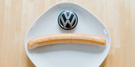 Eine Currywurst mit Aufschrift "Volkswagen Originalteil" und ein VW-Logo liegen auf einem Teller