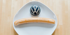 Eine Currywurst mit Aufschrift "Volkswagen Originalteil" und ein VW-Logo liegen auf einem Teller