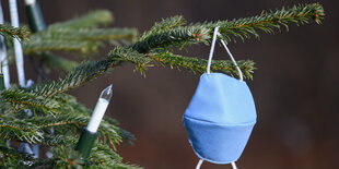 Ein Christbaum, an dem neben elektrischen Kerzen eine Maske hängt.