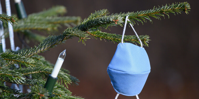 Ein Christbaum, an dem neben elektrischen Kerzen eine Maske hängt.