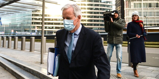 Michel Barnier mit Mundschutz und Aktenordnern unterm Arm. Im Hintergrund ein Kamerateam, das ihn von hinten filmt