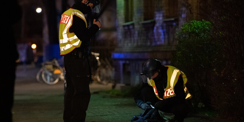 Zwei Polizisten begutachten auf einem Bürgersteig den Inhalt einer Tasche.