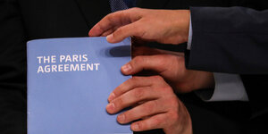 Drei Hände halten eine Kopie des Pariser Klimabkommens