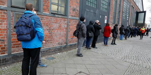 Menschen stehen in einer Schlange vor einem Backsteingebäude