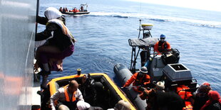 Eine Frau klettert aus einem Rettungsboot an Bord eines Schiffs.