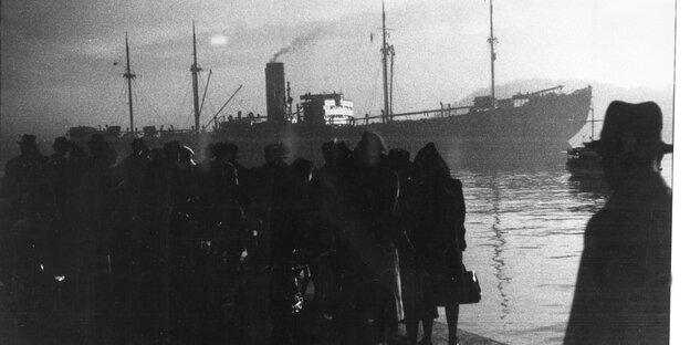 Dicht gedrängt stehen Menschen im Hafen am Wasser in dem schwarzweißen Bild