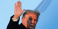 Trump hebt die Hand und winkt zum Abschied, sein Gesicht erscheint orange