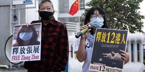 Zwei Menschen mit Protestschildern sthen vor einem Gebäude mit gehisster China Flagge