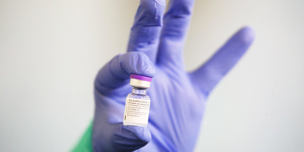Eine Hand mit blauem Handschuh hält eine Impfdosis hoch