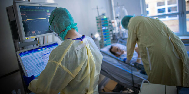 Medizinisches Personal in Schutzkleidung auf einer Krankenhausstation kümmert sich um einen Patienten