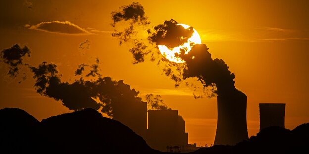 Die Silhouette eines Kohlekraftwerks zeichnet sich im Gegenlicht der untergehenden Sonne ab