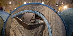 Ein Mann mit Mund-Nasenmaske schaut aus einem Zelt heraus.