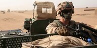 Ein mit Helm, Tuch und Brille vermummter Soldat in Flecktarn sitzt in einem Panzerfahrzeug