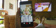 Ein Mann hält ein Smartphone in der Hand - auf dem Bildschirm zeigt ein Kleiner Junge über Videochat seine grün bemalten Hände