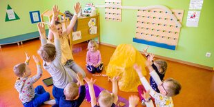 Kindergartenkinder sitzen mit Erzieherin im Kreis