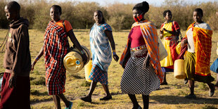 Frauen mit bunten Gewändern und Kanistern unterwegs.