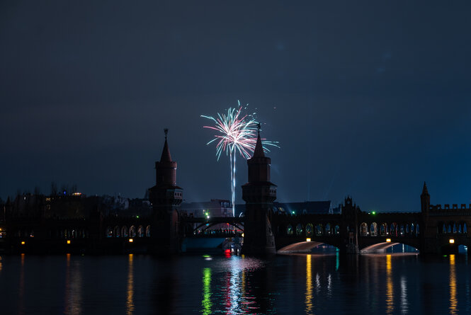 Eine Silvester-Rakete explodiert über der Oberbaumbrücke. Ansonsten ist der Himmel dunkel und leer.