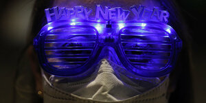 Eine Frau mit einer Mundschutzmaske trägt eine beleuchtete Brille, auf die die Worte "Happy New year" angebracht sind.