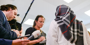 Journalisten interviewen einen Frau, die mit dem Rücken zur Kamera steht und ein Kopftuch trägt
