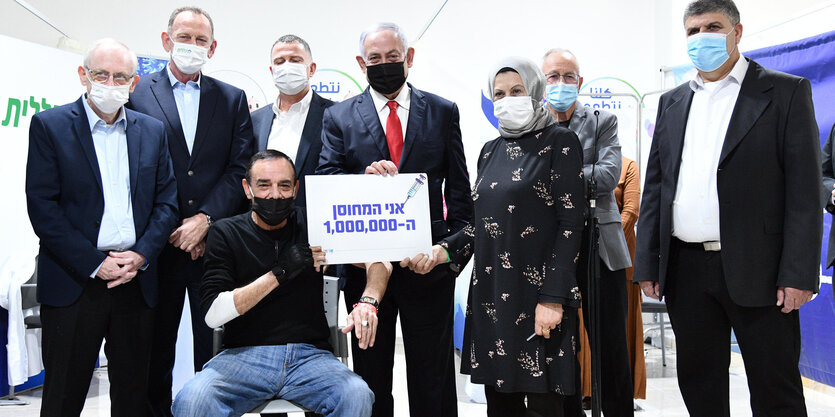 Ein Mann mit einem Schild, auf dem 1.000.000 steht, vor Menschen mit Masken