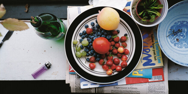 Ein Teller voll Obst, Trauben, Heidelbeeren, Erdbeeren und Äpfeln steht auf einem Fensterbrett