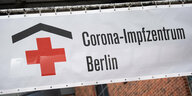 Das Bild zeigt das Symbol des Deutschen Roten Kreuzes neben einem auf das Impfzentrum hinweisenden Schriftzug auf einem Banner am Eingang des Gebäudes.