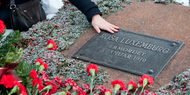 Eine Person legt ihre Hand auf eine Plakette an der Gedenkstätte der Sozialisten auf dem Lichtenberger Zentralfriedhof