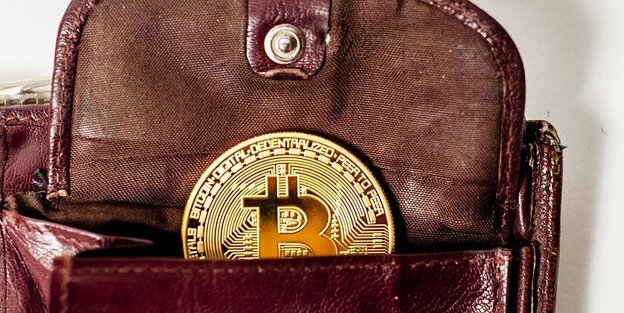 Ein offener Geldbeutel mit einer Bitcoin Münze liegt auf einer weißen Fläche