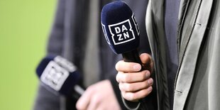 Nahaufnahme von zwei Händen, die ein Mikrofon mit der Aufschrift Dazn in der Hand halten