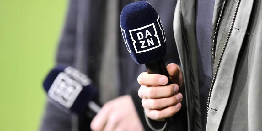 Nahaufnahme von zwei Händen, die ein Mikrofon mit der Aufschrift Dazn in der Hand halten