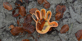 Ein Plastikförmchen in Form einer Hand liegt in einem Sandkasten