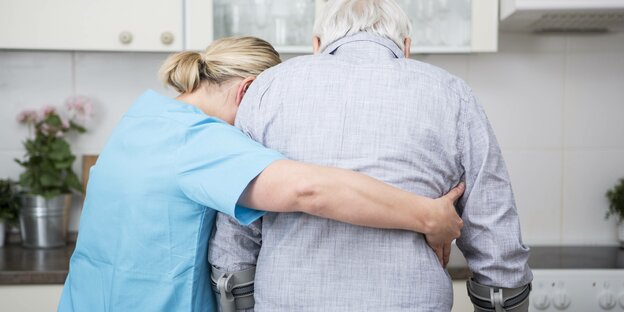 Eine Pflegekraft stützt einen älteren Mann auf Krücken in seiner Küche