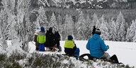 Wintersportler sitzen am Sonnenberg im Harz auf ihrem Schlitten und machen Pause.